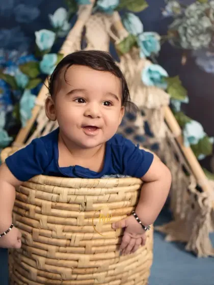 A happy baby boy peeks out of a wicker basket, showing off his cheerful personality.