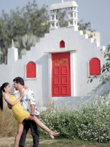A classic romantic dance pose from a pre-wedding shoot. The groom lifting the bride against the backdrop of a beautiful white building creates a dreamy, fairytale-like image.