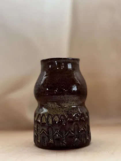 A dark, richly glazed vase with intricate carvings around the base. The texture is incredible.