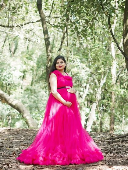 This vibrant magenta gown stands out beautifully in a forest setting. Its full tulle skirt creates a classic princess silhouette for a memorable maternity shoot.