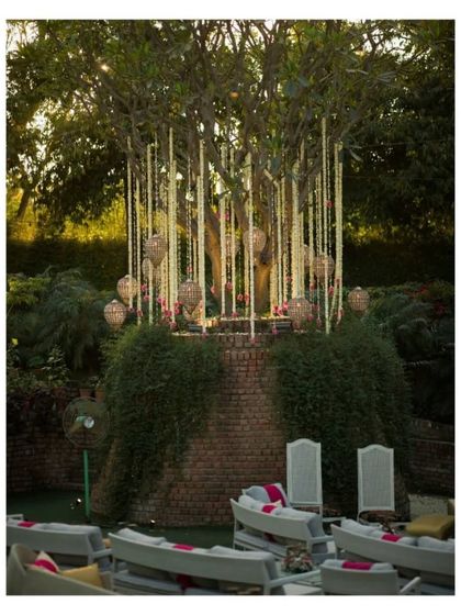 A beautifully decorated tree with hanging floral strings and lanterns, creating a magical seating area for an outdoor wedding function.