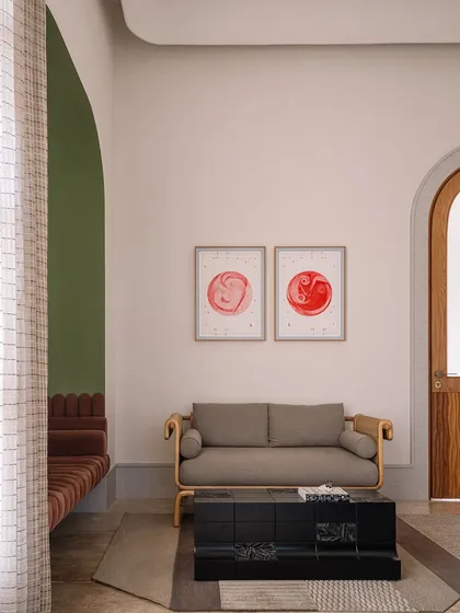 The home office at Rehethaan is bathed in morning sunlight. The space features a comfortable seating area with a sofa nestled in an olive-green archway, creating a perfect spot for breaks between work.