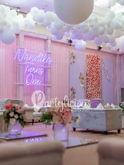 Floating on a cloud. For this first birthday, we created a dreamy ceiling installation with fluffy white balloon clouds and a custom neon sign, making the whole room feel ethereal and magical.