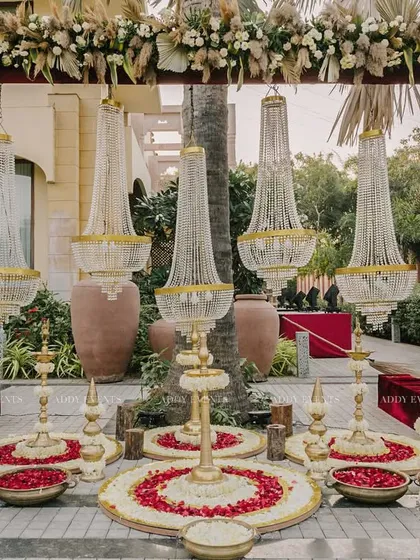 A majestic entrance designed for a day wedding. This setup combines the grandeur of suspended chandeliers with the rustic charm of pampas grass and a traditional floral rangoli.