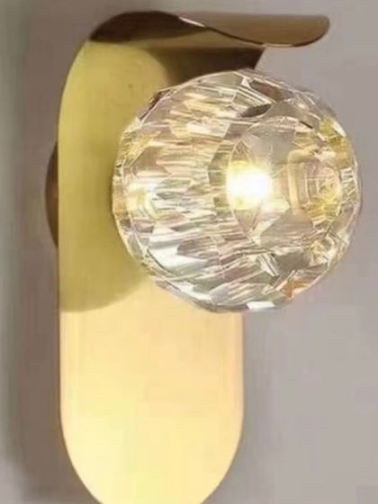 A close-up of a wall sconce with a faceted crystal globe. The crystal refracts the light, creating a beautiful, sparkling effect.
