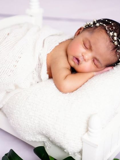 A sleeping newborn looking like royalty on a tiny white bed prop. I use only the safest, professional lighting for all my baby shoots.
