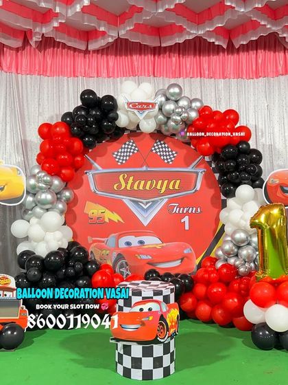 A high-energy Disney Cars theme for Stavya's first birthday. This setup features a custom backdrop, character cutouts of Lightning McQueen, and a red, black, and silver balloon arrangement.