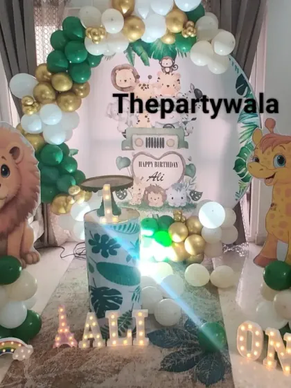 A cozy jungle theme setup for a home party. The green and gold balloon arch with cute animal cutouts fits perfectly in a living room space.