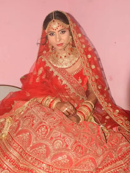 A full shot of the bride in her red and gold lehenga. The makeup is classic and regal, fitting for a wedding ceremony.
