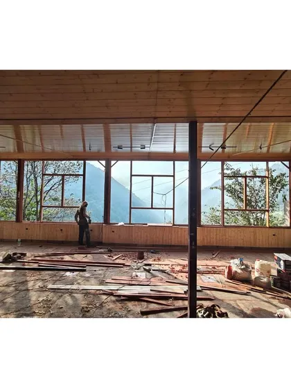 A worker inside the unfinished pavilion, with the vast mountain landscape visible through the window frames. This shot highlights the scale of the view that the architecture is designed to capture.