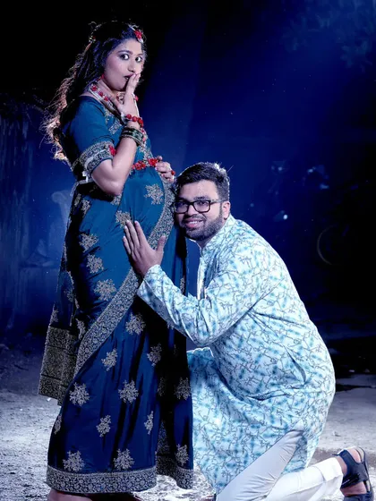 A dramatic and playful studio-style maternity portrait. The father-to-be leans in to listen to the baby bump, creating a fun and memorable image for the couple.