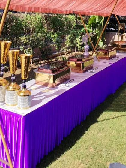 A colorful and festive buffet setup for a daytime garden party. The bright purple table skirt and golden decorative vases add a pop of color, making the food station a cheerful focal point.