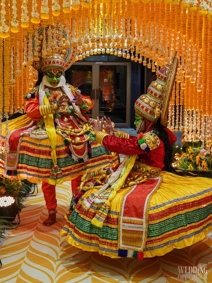 A unique cultural element featuring Kathakali dancers as part of the welcome for a Haldi ceremony. Their vibrant costumes complement the yellow and orange floral decor perfectly.