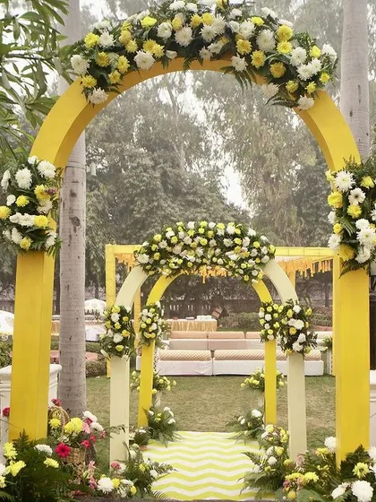 A classic yellow floral archway welcomes guests to a traditional Haldi ceremony, set in a beautiful garden. The bright yellow is cheerful and perfectly suited for the occasion.