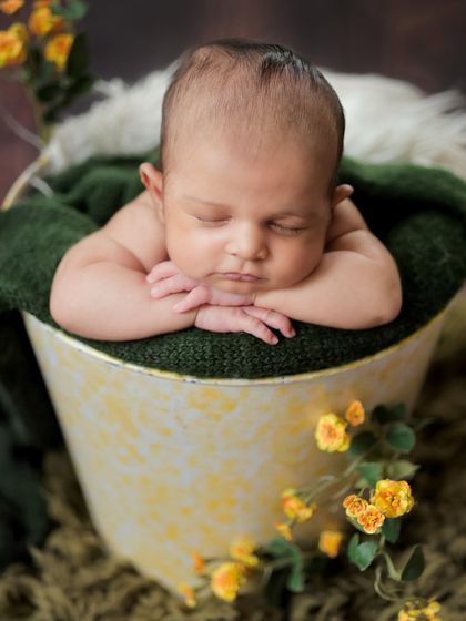 The classic "chin on hands" pose is a favorite for newborn photography. This little one looks so peaceful resting in a bucket surrounded by yellow flowers.