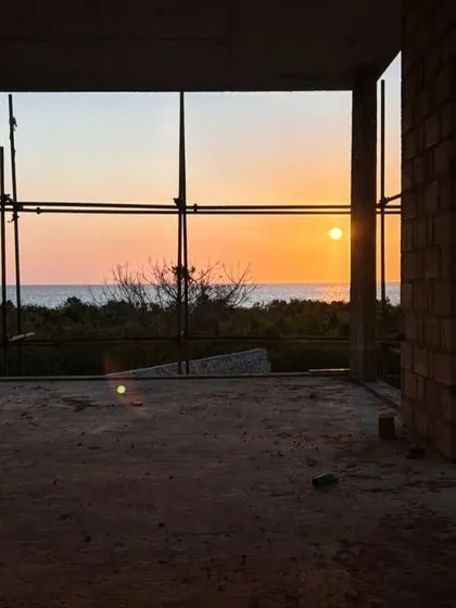The sun sets through the scaffolding of the Kizikula project. Even during construction, the building's fundamental connection to its stunning coastal location is evident.