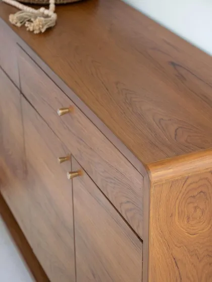 A detail shot of the 'Marshall' shoe cabinet, showing the smooth, curved corner and the warm grain of the teak wood.
