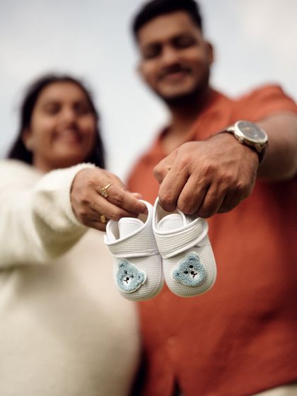 A close up shot of the couple holding a pair of tiny baby shoes. The focus is tight on their hands and the shoes, making it an intimate and symbolic announcement.