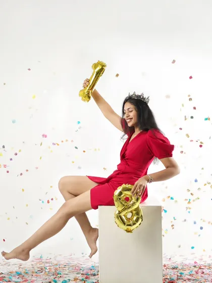 "I can't keep calm, it's my 18th birthday!" This young woman is celebrating in style, wearing a crown and a vibrant red dress, surrounded by confetti.