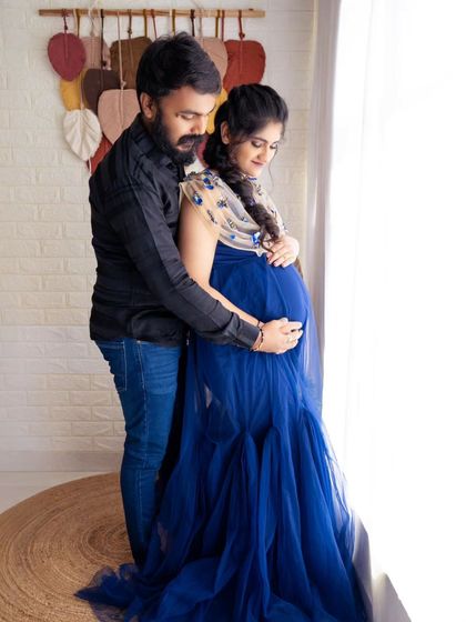 A tender moment by the window, with the partner embracing the mom-to-be from behind as they look out together.