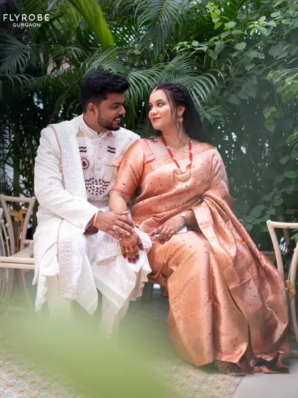 A sweet moment between a couple. She is wearing a beautiful peach silk saree, while he is in a classic white sherwani.