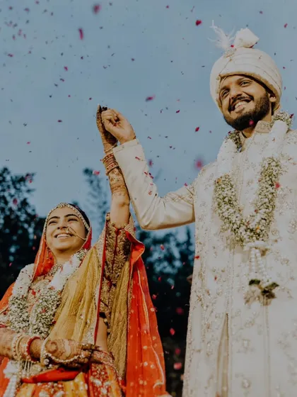 A triumphant moment for Nidhi and Jay as they raise their hands after the wedding ceremony, with petals raining down on them.