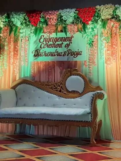 A stage setup for the engagement ceremony of Dhirendra and Pooja, featuring a classic sofa against a backdrop of colorful drapes and lighting.