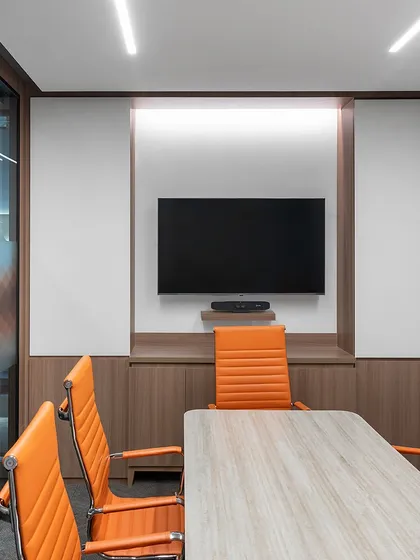A meeting room in the TajSATS office, designed with bright orange chairs and acoustic wall paneling. The room is equipped with a large screen and integrated writing surfaces, making it a highly functional space for team collaboration.
