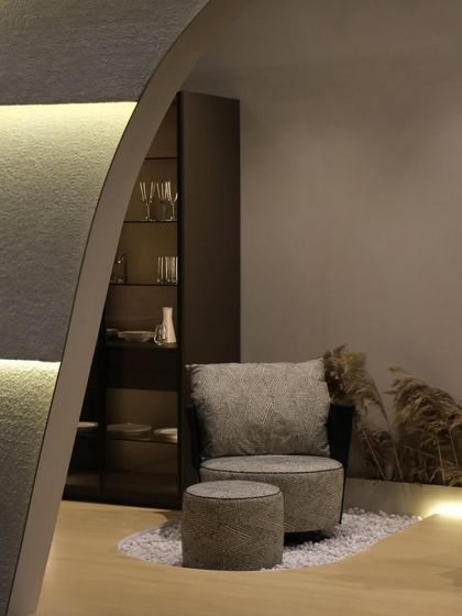 A close-up of the armchair and footstool inside the booth. The soft, textured fabric of the furniture is echoed in the bouclé wall finish, creating a cohesive and tactile environment.