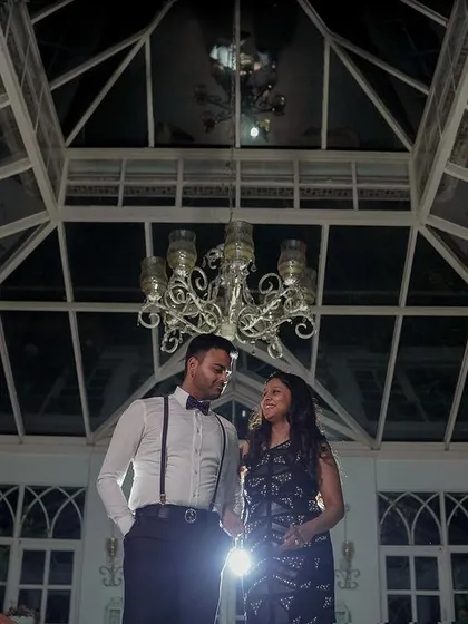 A wide-angle shot of a couple during their pre-wedding shoot inside a beautiful glasshouse. The architectural details and dramatic lighting create a sophisticated and elegant atmosphere.