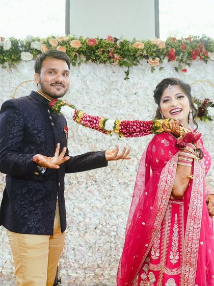 A playful moment between the happy couple. Her bright pink lehenga and his navy Jodhpuri suit make for a vibrant and joyful wedding day look.