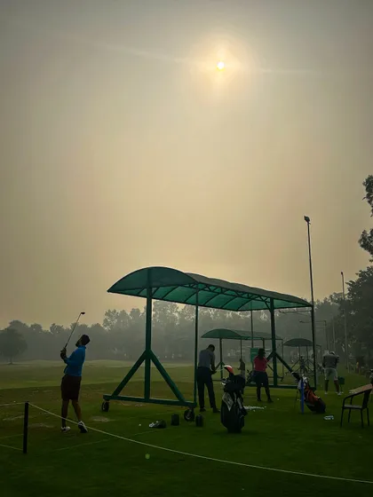 A golfer takes a swing under the hazy sun, with a portable canopy providing some shade.