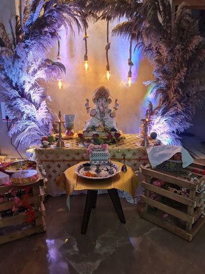 A rustic-chic Ganpati decoration using pampas grass arches and hanging Edison bulbs. This trendy and earthy design offers a unique alternative to traditional floral setups.