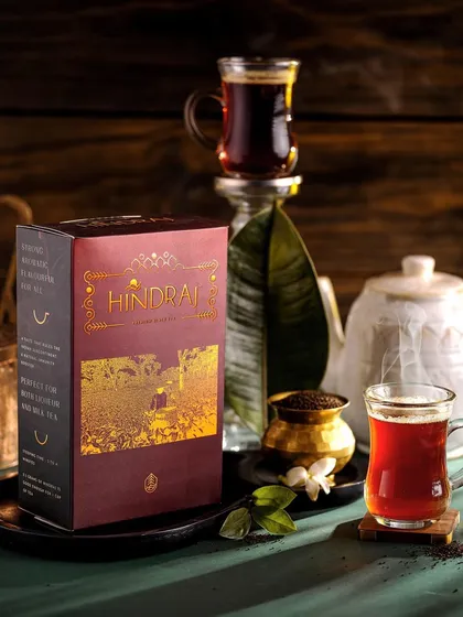 Another elegant shot of Hindraj black tea, focusing on the rich red color of the brew. The composition with a traditional teapot and jasmine flowers creates a serene and timeless image.