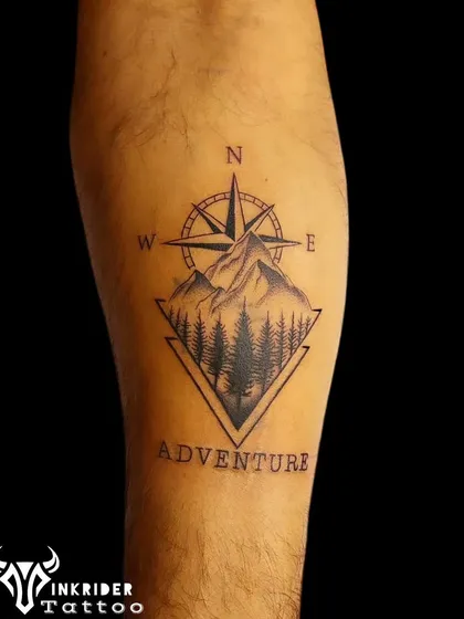 A bold "ADVENTURE" tattoo featuring a compass, mountains, and a forest. This design is for the true explorer at heart.