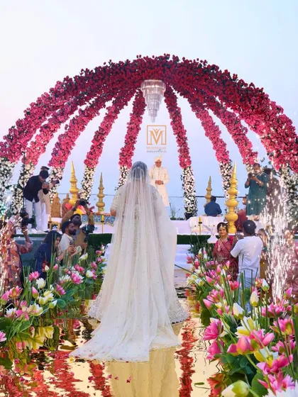 A bride's grand entrance to a stunning sea-facing mandap. The aisle is designed with a mirrored surface and floating lotuses, creating the illusion of walking on water towards a floral dome.