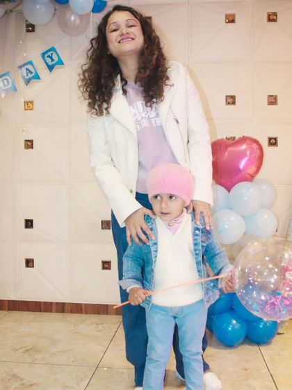 A mother and child pose for a full-length shot at a birthday party, showing off their coordinated casual outfits.