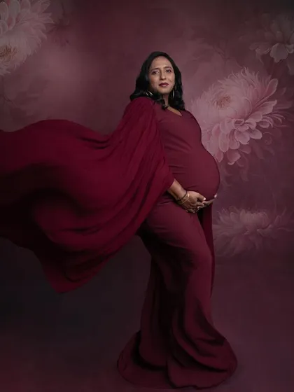 A dramatic profile shot with the red gown flowing behind her. The rich color and the floral painted backdrop create a very artistic and high-fashion look.