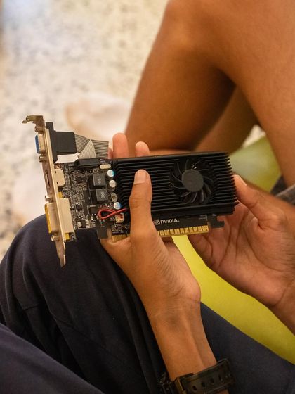 A child holds a graphics card, examining its structure. Before we build, we always take time to understand each component, from the fan and heat sink to the PCI connector.