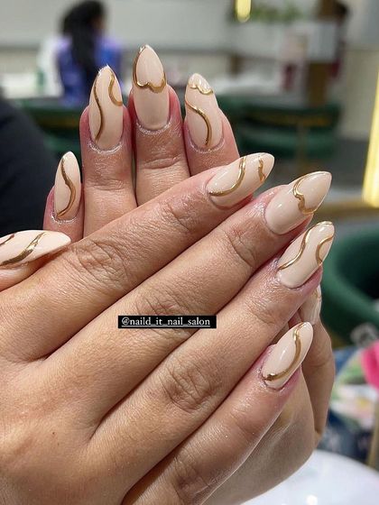 A chic and minimalist design featuring a solid nude base on almond nails. Delicate, hand-drawn gold chrome swirls add a touch of sophisticated sparkle.