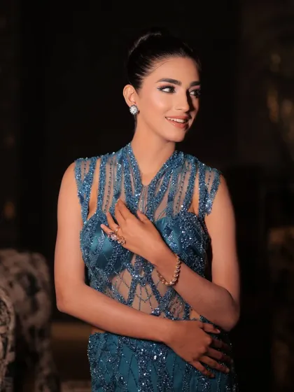 A smiling portrait in the blue gown. The styling is designed to be both glamorous and approachable.