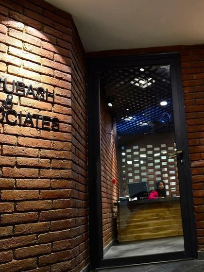 The entrance to the Subash & Associates architect's office, where a single downlight grazes the exposed brick wall. This simple technique highlights the texture of the material and the firm's logo, creating a dramatic and confident first impression.