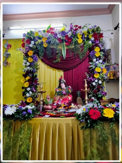 A multi-colored floral arch against a backdrop of yellow and maroon curtains. This home Ganpati decoration uses a wide array of flowers like gerberas and roses to create a joyful and celebratory look.