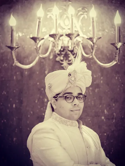 A classic groom portrait with a vintage, royal feel. The warm, focused lighting on the groom's sherwani and sehra, set against the ornate candelabra, creates a timeless and regal image that honors tradition.