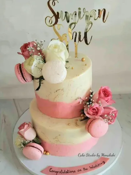 This two-tiered wedding cake is a beautiful example of my completely fondant-free work. It features a textured pink and white buttercream finish, adorned with fresh roses and delicate pink macarons for a touch of elegance.