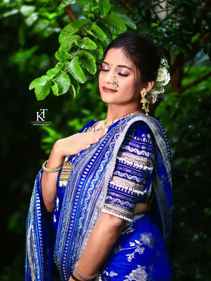 A serene outdoor shot of a bride in a royal blue Paithani saree. The natural light highlights the flawless makeup and the intricate details of her attire.