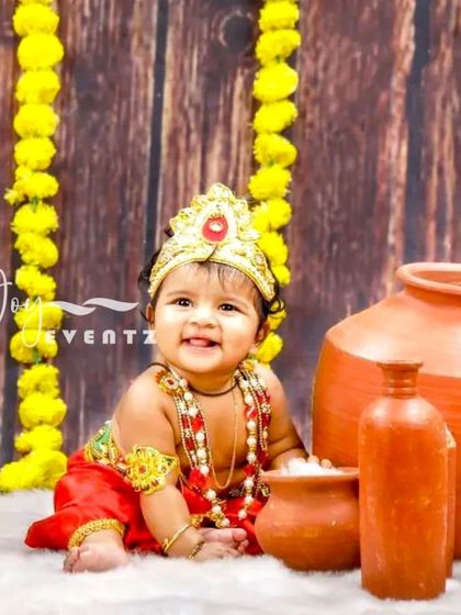 A joyous Little Krishna themed photoshoot captures the essence of the festival. The baby, dressed as Krishna, smiles brightly amidst traditional props like clay pots and marigold flowers.