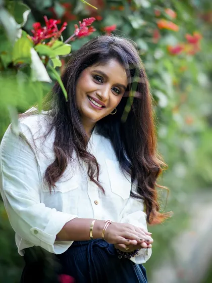 A lovely portrait of a woman with a warm smile, posing amidst beautiful red flowers during her outdoor session.
