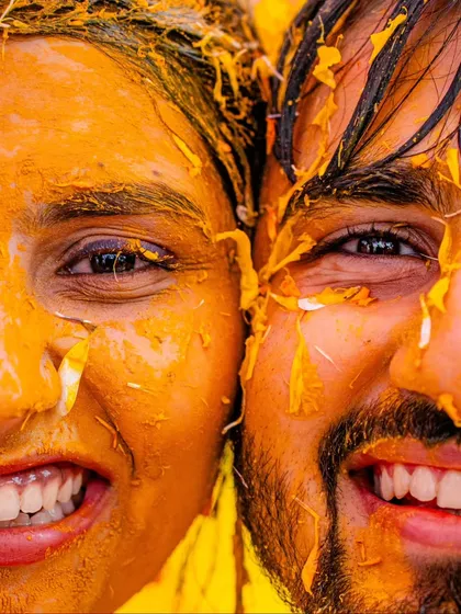 A super close-up shot capturing the happy, turmeric-covered faces of the bride and groom. This image is all about the texture, the vibrant color, and the infectious smiles.