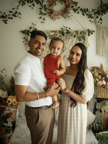 A warm and welcoming family portrait. The family of three stands together, their coordinated neutral outfits perfectly complementing the earthy tones of the boho studio.
